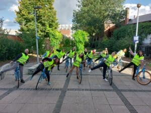 Group of women in bright vests on bicylces leading to one side with one leg in the air.
