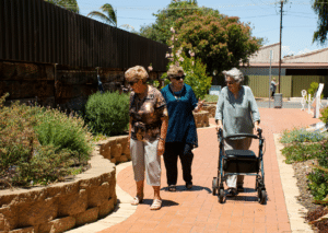 Three older women walking in a park, one with a walker