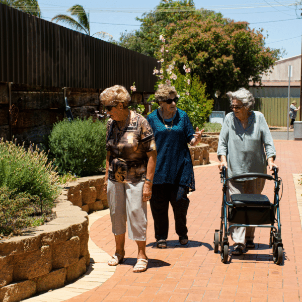 Three older women walking in a park, one with a walker